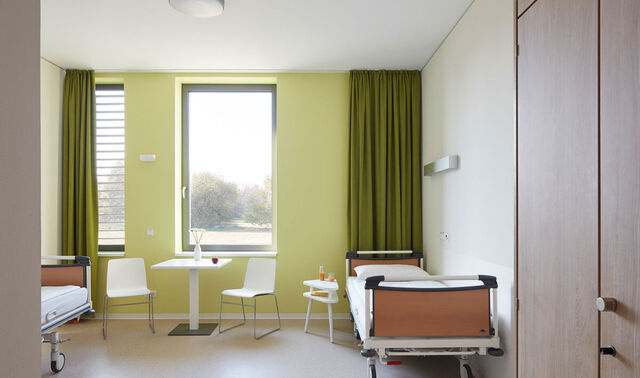 Patientenzimmer mit zwei Betten in der Klinik Königshof. Zwischen den zwei Betten befindet sich noch ein kleiner Tisch mit zwei Stühlen in dem Zimmer.