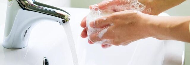 Hände werden unter einen Wasserhahn gehalten.