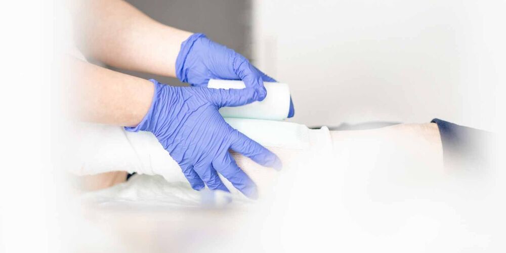 Eine Person, welche Hygienehandschuhe trägt legt einer anderen Person einen Verband an.