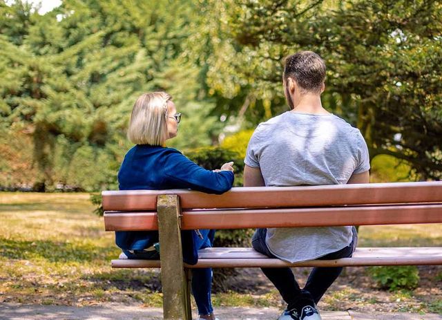 Ein Mann und eine Frau sitzen in einem Park auf einer Bank und unterhalten sich. 