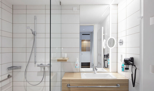 Badezimmer eines Privatzimmers mit einer Dusche, einem Waschbecken, einem Spiegel und einem Föhn.