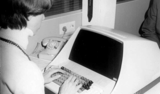 Eine Frau sitzt an einem Schreibtisch und tippt auf einem der ersten Computer.